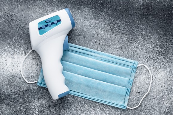 An infrared thermometer and a surgical mask lying on concrete.