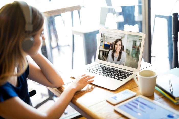 Woman wearing headphones and participating in a video conference call on a laptop in a cafe.