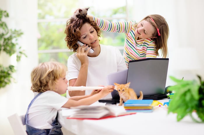 Woman at laptop on phone while young girl pulls her hair and young boy plays plastic flute