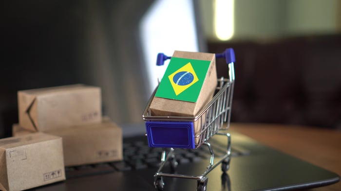 A miniature shopping cart with packages adorned with the Brazilian flag on top of a computer.