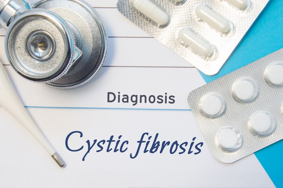 A report saying "cystic fibrosis diagnosis" is shown along with two packages of pills.