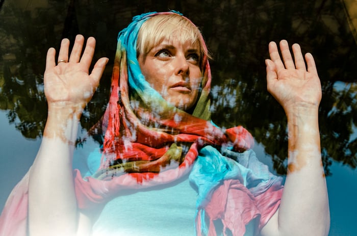 A woman in a scarf behind a window, looking bored, with her palms against the glass.