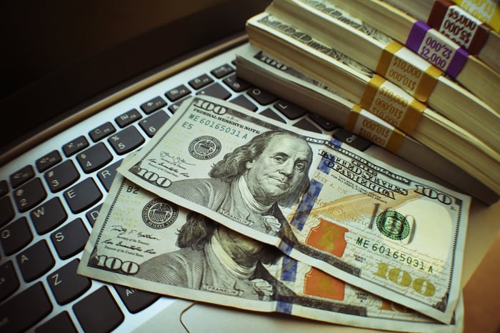 Stacks of cash and a couple of separate hundred-dollar bills, all on top of a laptop computer.