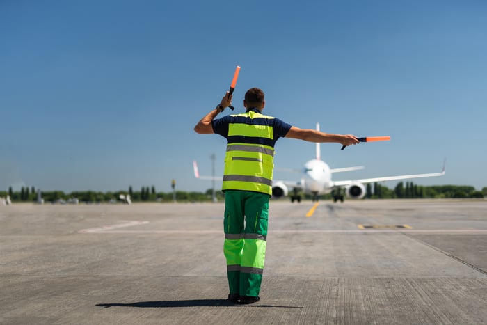 An airline ground crew worker points an aircraft towards the terminal.