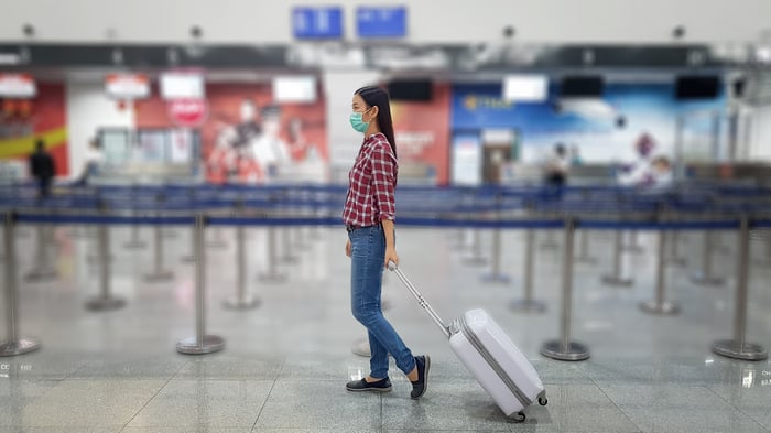 A traveler in a mask walking through an airport terminal.