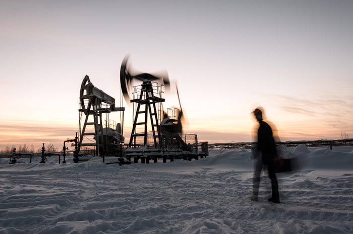 Oil pumps in motion with a person walking by and snow on the ground.