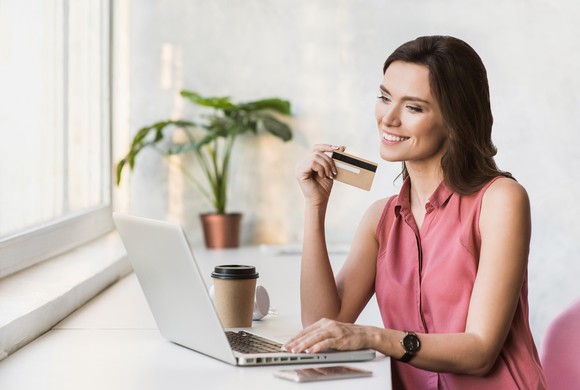 Smiling woman holding a credit card while sitting in front of a laptop