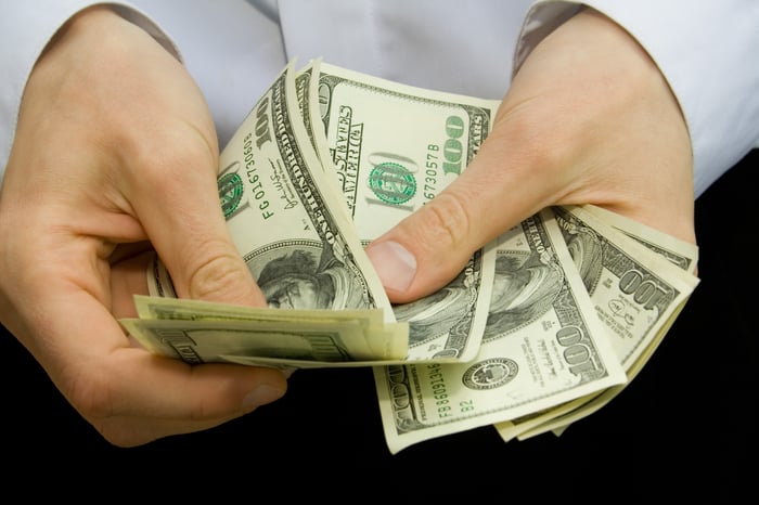 A person counting a stack of one hundred dollar bills in his hands.