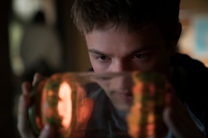 A young man looking at a glowing object inside a small jar.