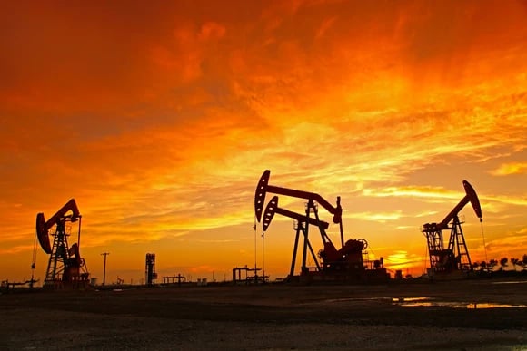 Several oil pumps against an orange sky near sunset.