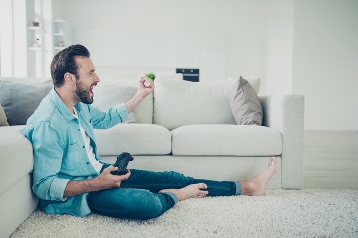 A man having a good time playing a video game while sitting on the floor.