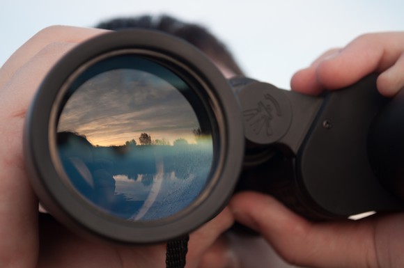 A person using binoculars to look into the horizon.