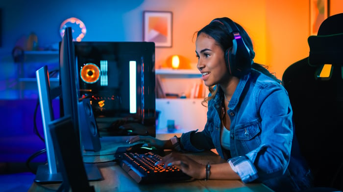 Smiling girl wearing headphones and playing a video game on her computer.