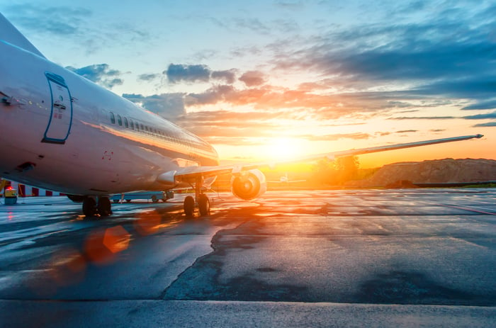 An airplane parked at an airport with the sun rising ahead.