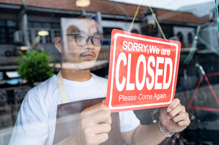 Man hanging sign in shop window saying sorry we are closed