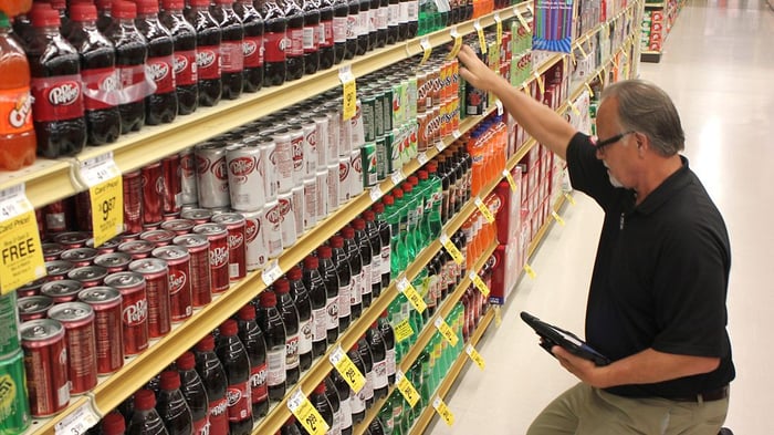 A man checking a grocery store shelf stocked with soft drinks.