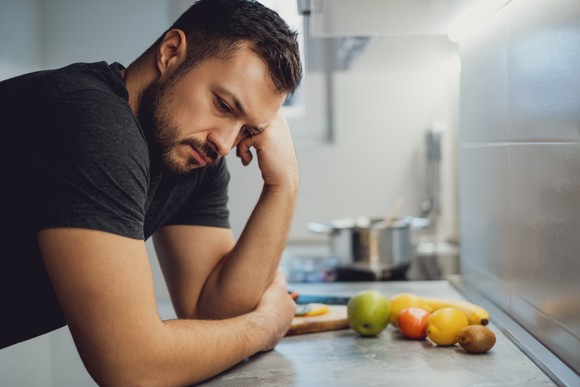 Man with somber expression leaning on kitchen counter