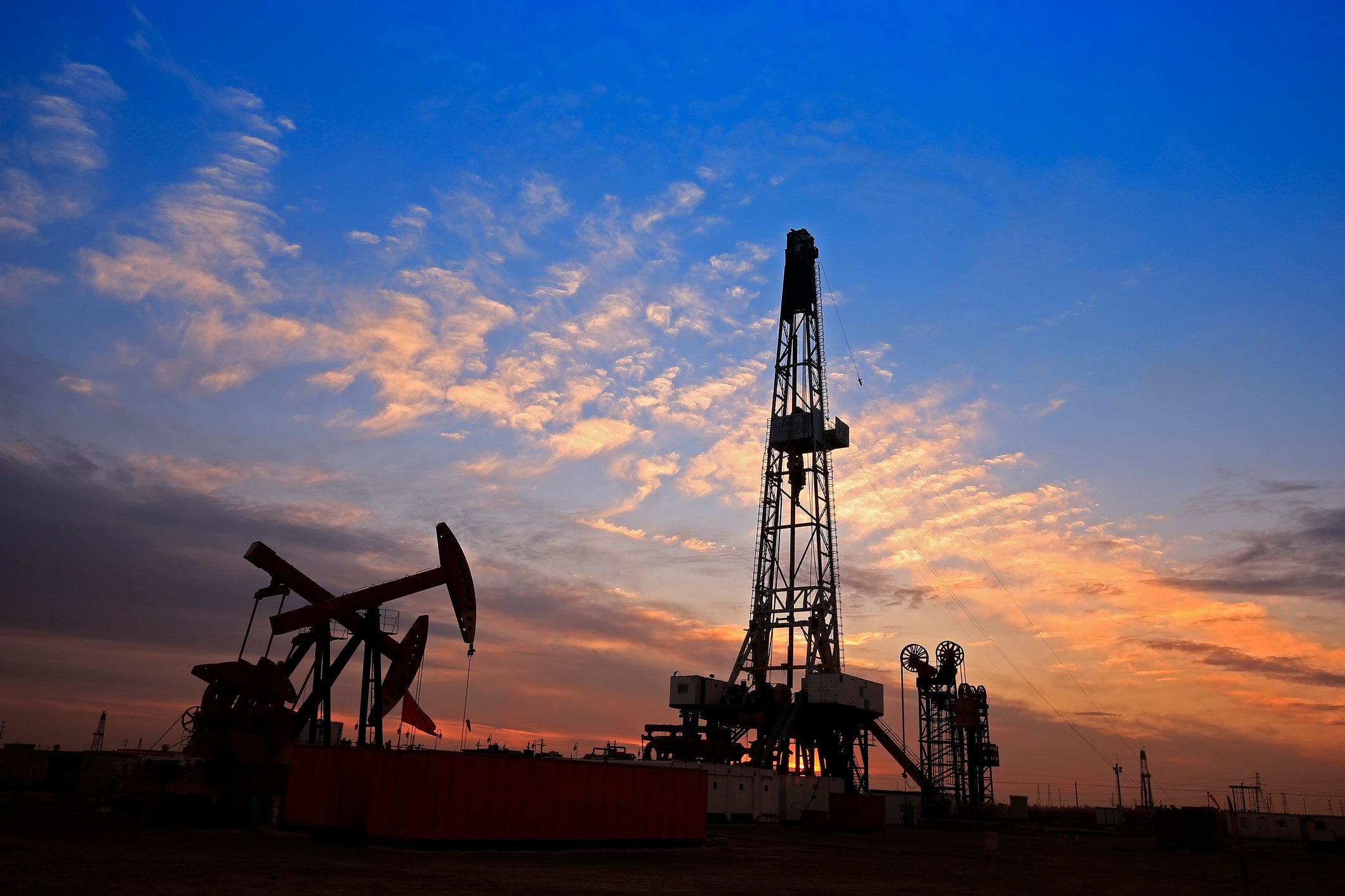 A drilling rig near some oil pumps with a nice sunset in the background.