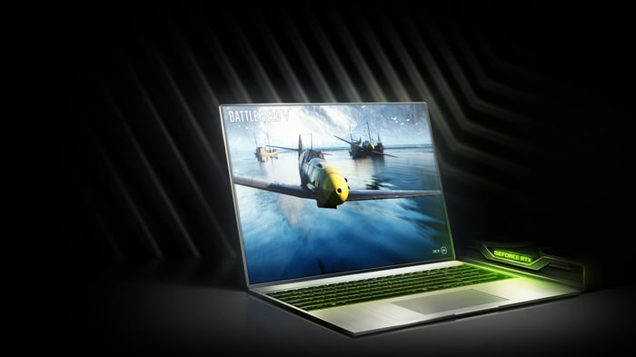 A laptop running a video game with an NVIDIA graphics card sitting to the side of the computer.