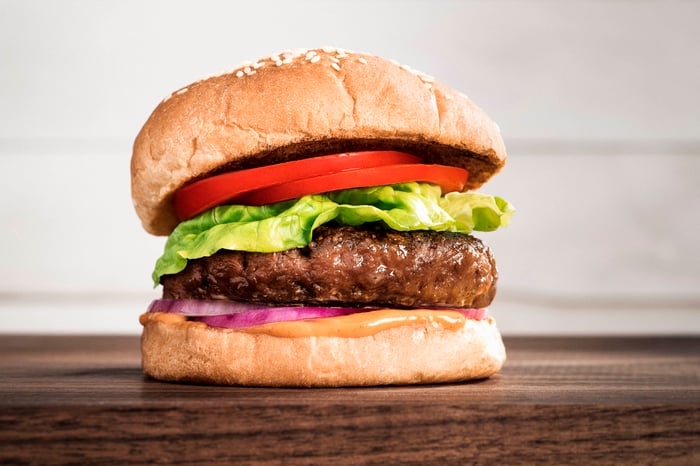 A Beyond Burger with cheese, lettuce, tomato, and opinion sitting on a wood surface. esittebey