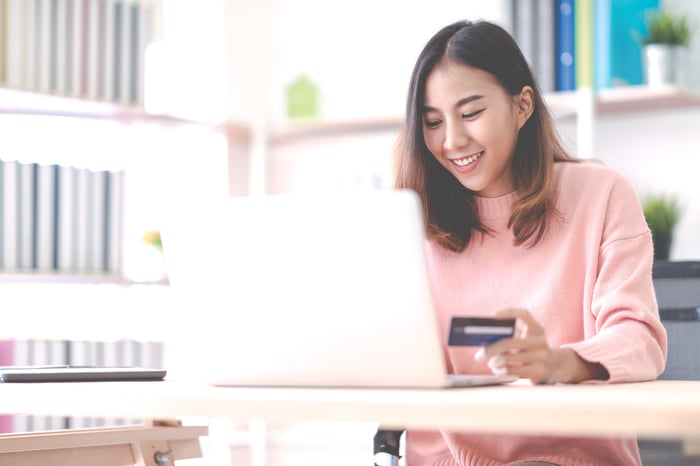 A young lady on her laptop holding a credit card in her left hand.