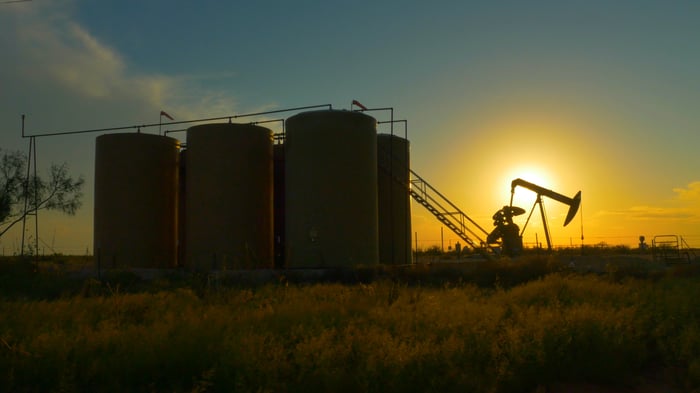 Oil storage tanks near a pumpjack and the sun in the background.