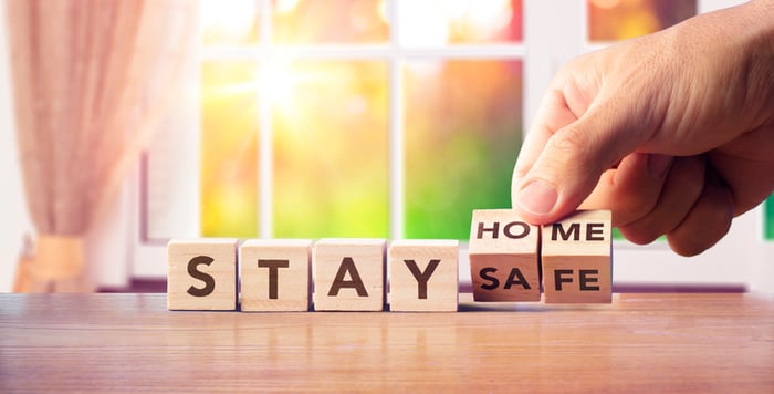 Person's hand turning over wooden cubes that say STAY HOME/SAFE.