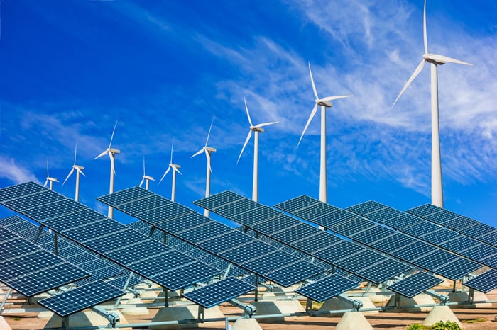 Solar panels and wind turbines under a blue sky.