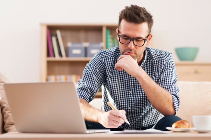 A man making notes as he looks at material on his laptop