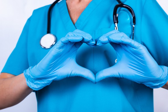 A doctor in scrubs holds up a heart with their hands