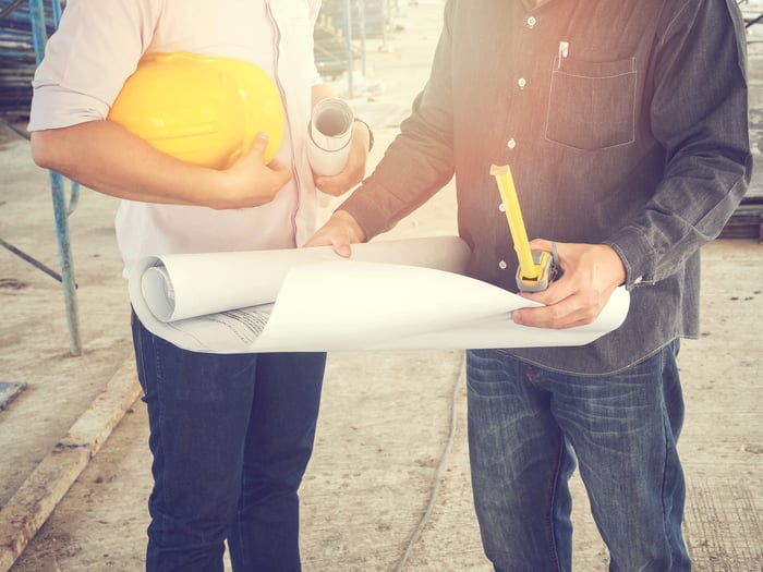 Two people looking at blueprints at a construction site