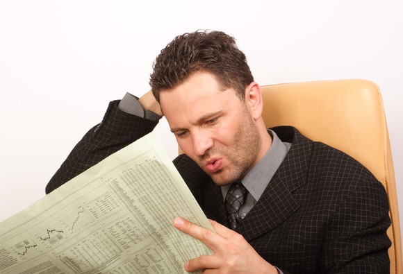 A visibly surprised man reading the financial section of the newspaper.