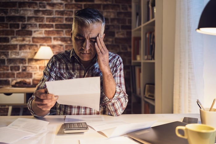 Older man at desk holding head while reading document