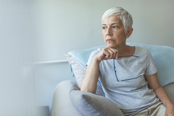 Older woman with serious expression sitting in chair holding eyeglasses