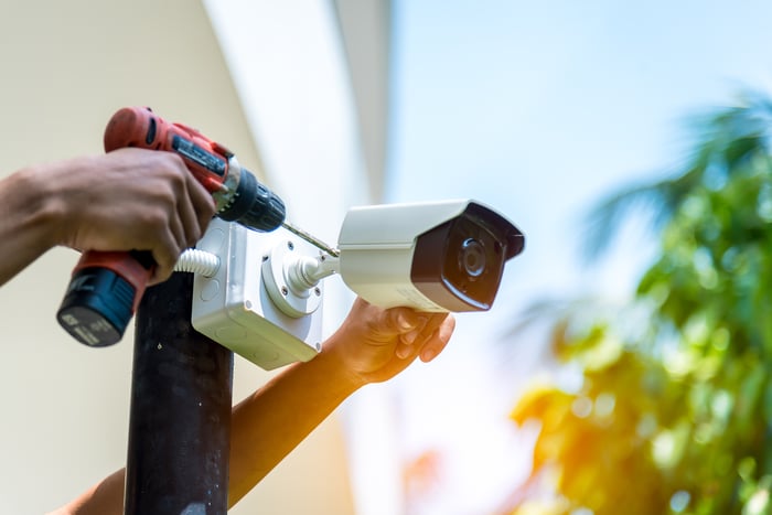 A person installing a security camera on a post with a drill