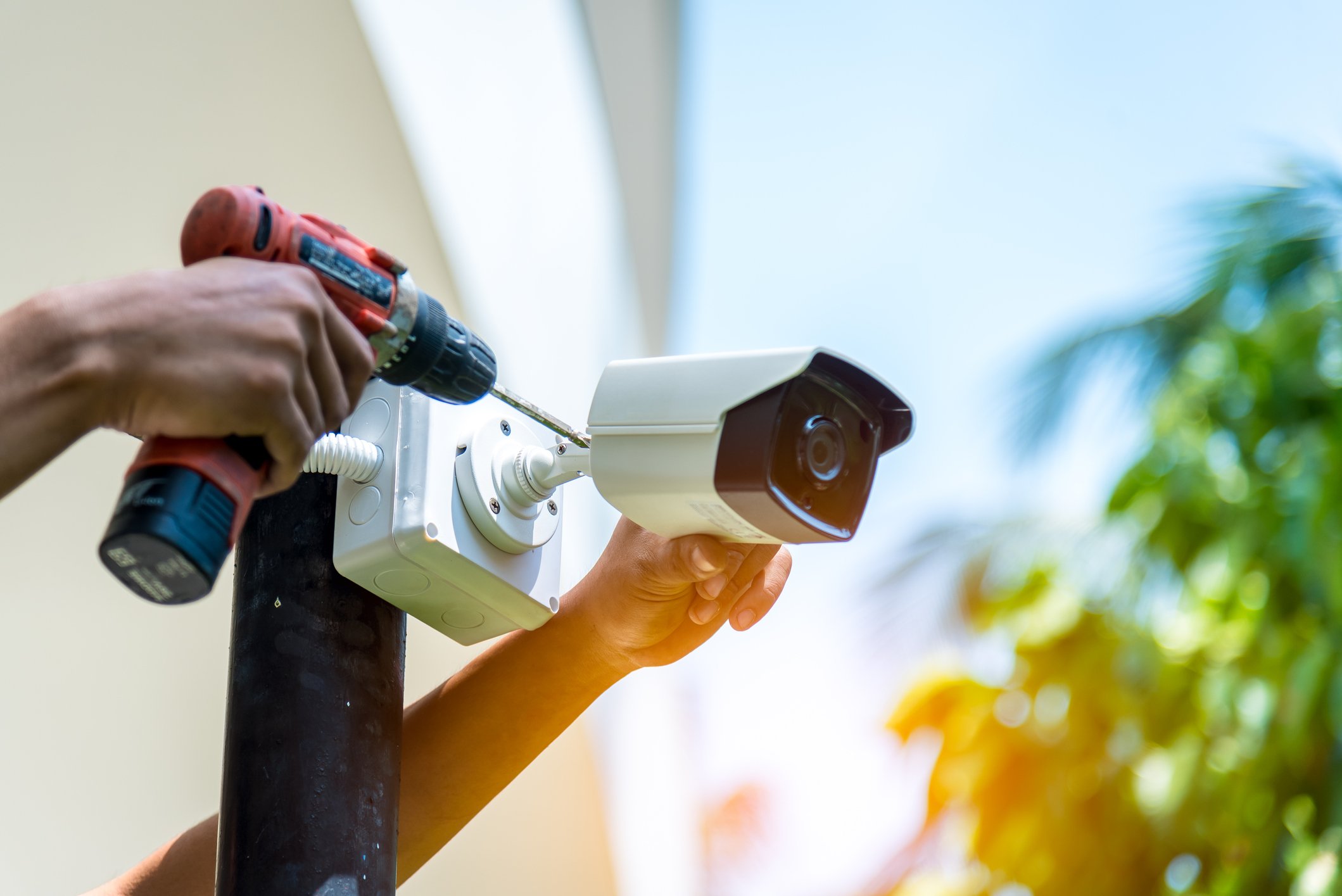 A person installing a security cameral on a post with a drill