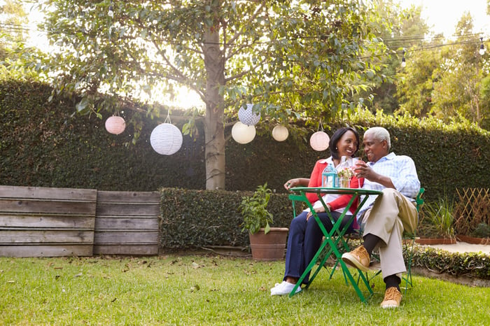 An older couple sitting on a lawn at a small table sharing drinks.