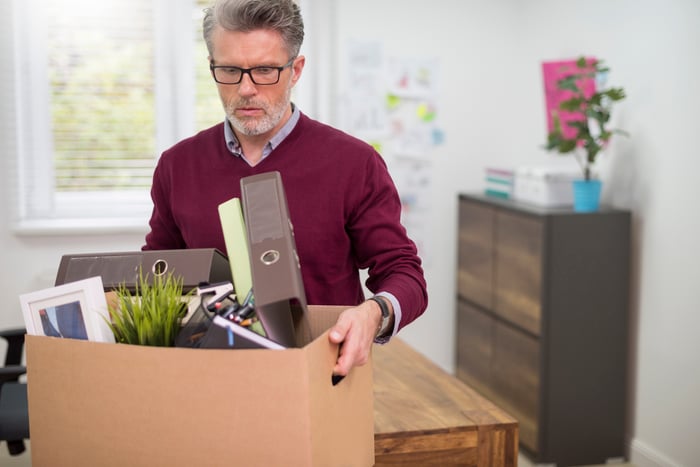 Older man holding large cardboard box of office supplies