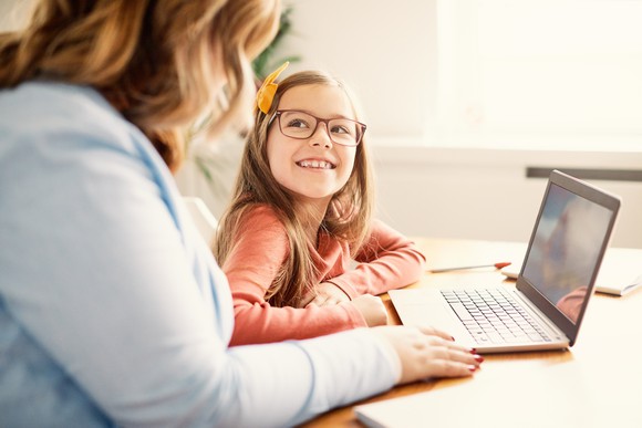 A smiling child looking at her mother, with an open laptop in front of them.