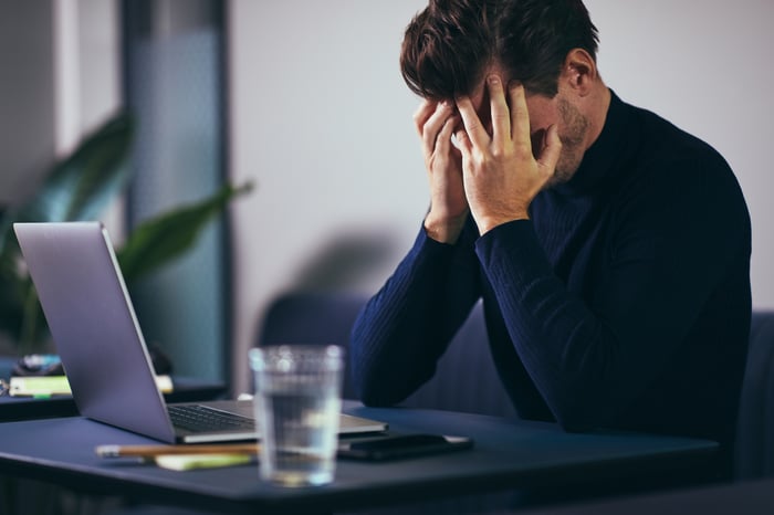 A man sitting in front of a laptop, covering his face