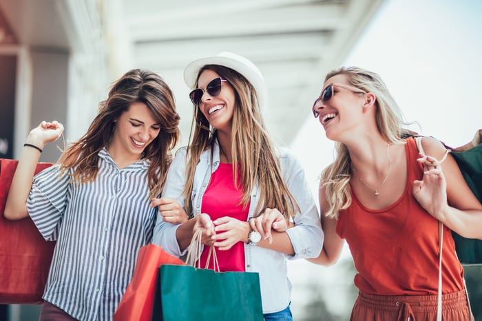 Three women with bags shopping in an outdoor retail area