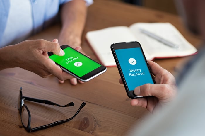 Two people holding cell phones transferring money.