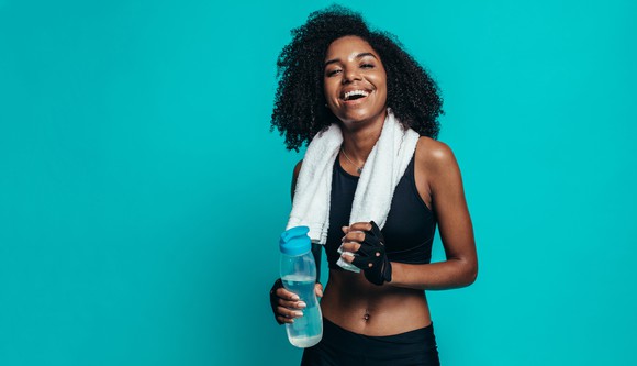 A young woman, with a towel around her neck, smiling and holding a water bottle.