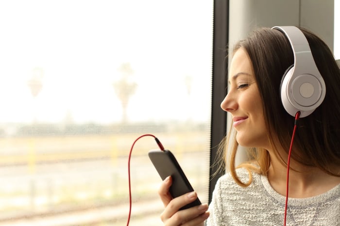 Person with headphones connected to mobile device near a window.