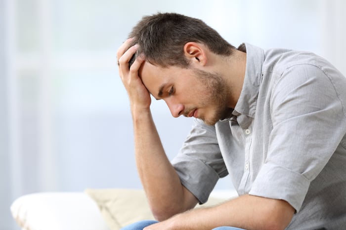 Man with sad expression holds his head in his hand.