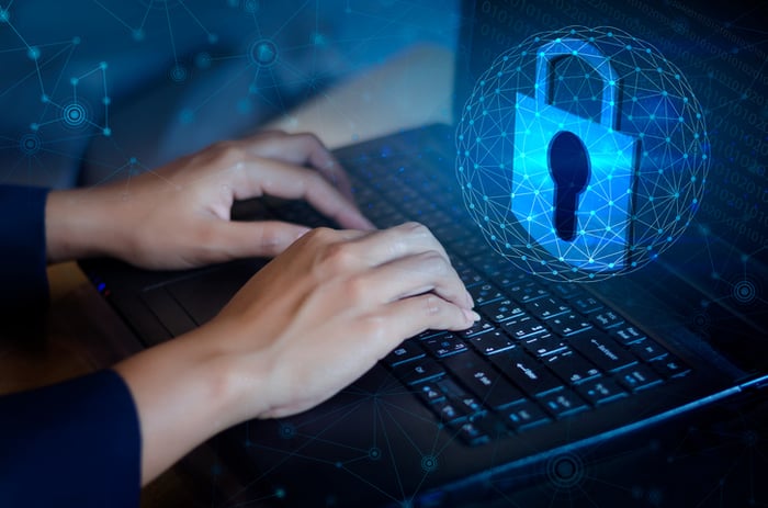 A digital padlock floating above a laptop that a woman's hands are typing on -- concept for cybersecurity.