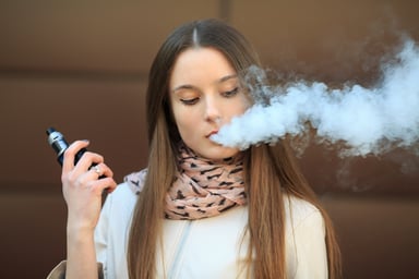 A girl holding a vape and exhailing a cloud of smoke