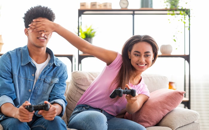 Two teens on a couch using hand controllers to play a video game. 