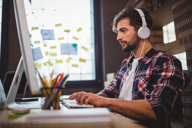 Young man at computer wearing headphones_GettyImages-658717670