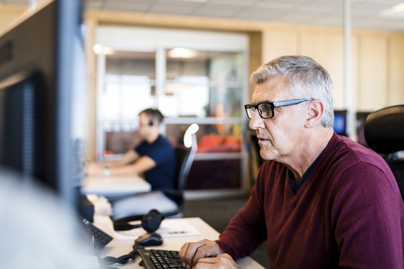 Older man typing on computer keyboard in an office.